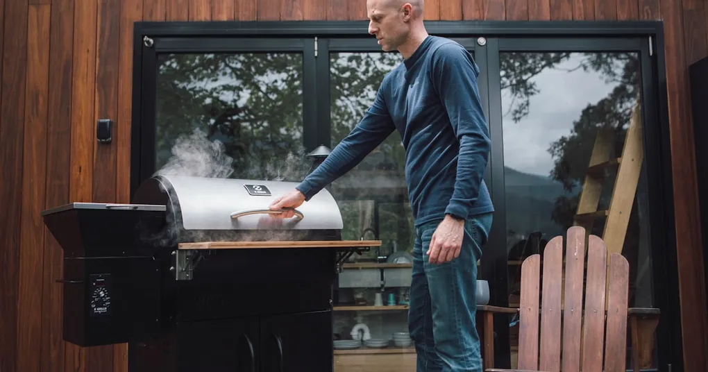 A sleek, modern outdoor pizza oven with a wood-fired interior, situated in a lush backyard